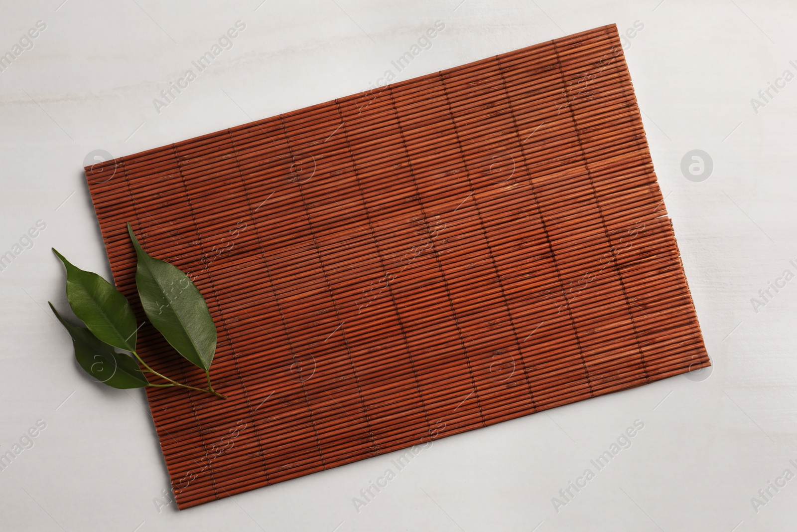 Photo of Bamboo mat and green leaves on beige table, top view. Space for text