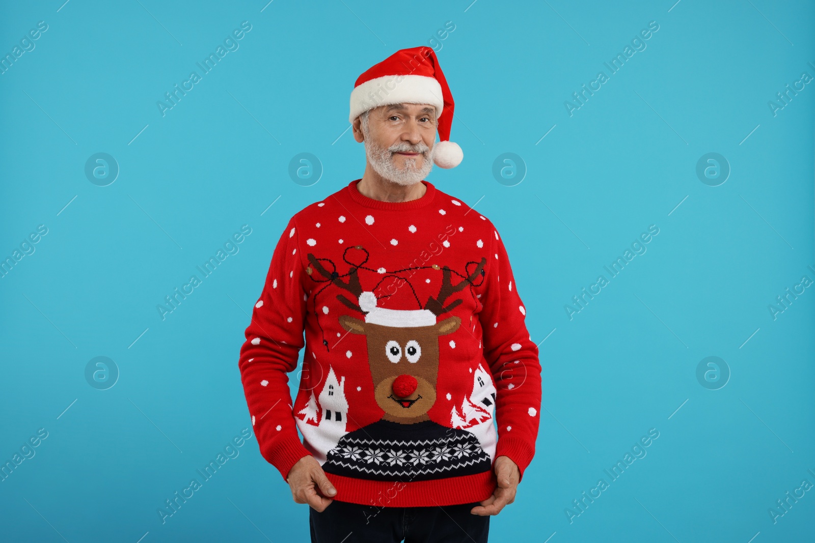Photo of Senior man in Christmas sweater and Santa hat on light blue background