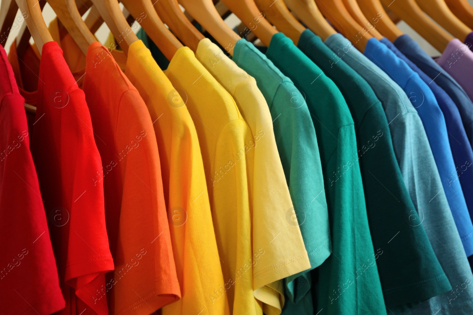 Photo of Hangers with bright clothes as background, closeup. Rainbow colors