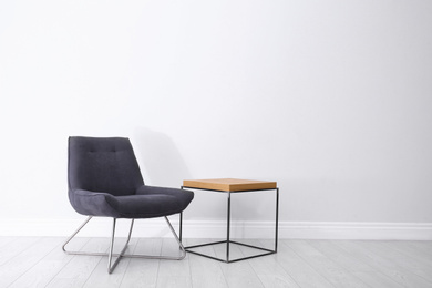 Photo of Comfortable armchair and table near light wall. Space for text