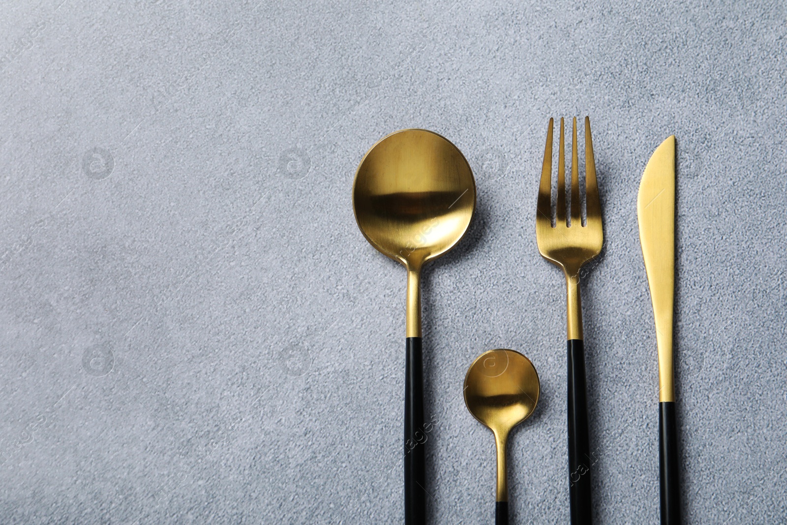 Photo of Stylish golden cutlery on grey table, flat lay. Space for text