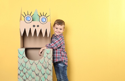 Photo of Cute little boy playing with cardboard dragon on color background. Space for text