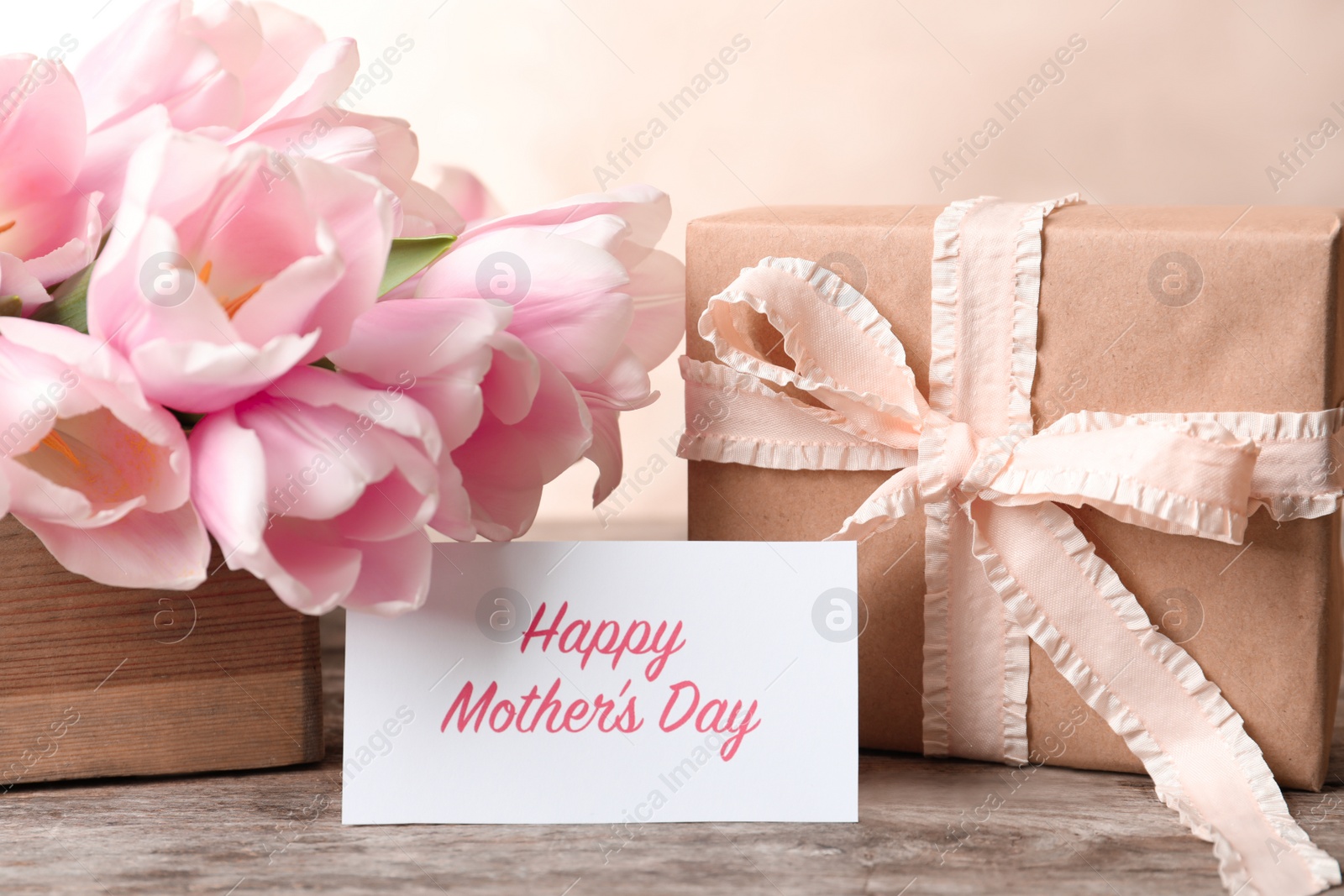 Photo of Greeting card with text HAPPY MOTHER'S DAY, tulips and gift box on table