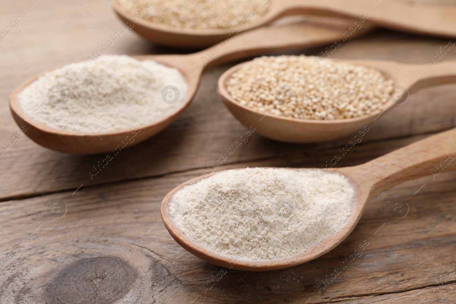 Photo of Spoons with quinoa flour and seeds on wooden table, closeup