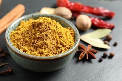 Photo of Dry curry powder in bowl and other spices on dark table, closeup