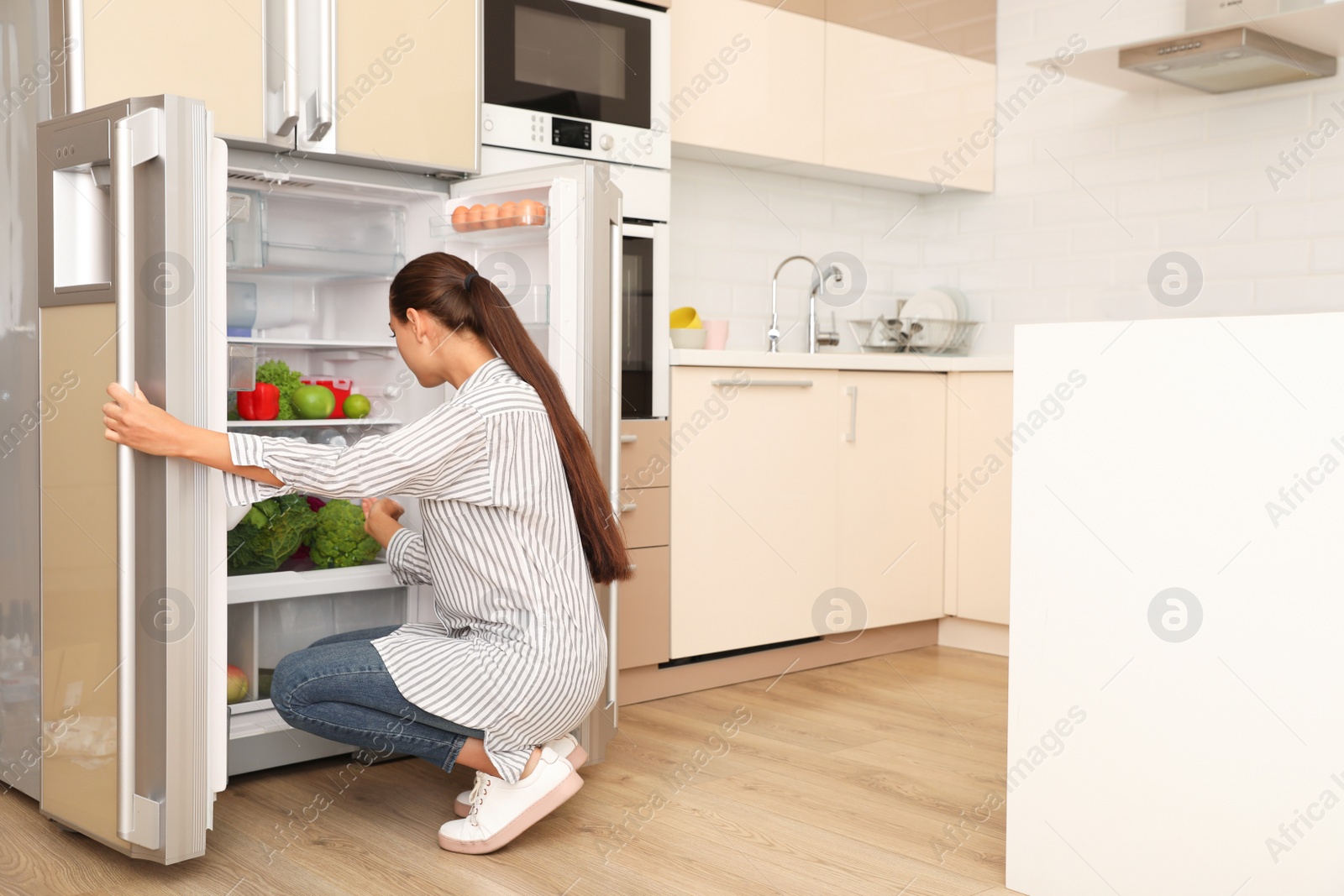 Photo of Young woman choosing products from refrigerator in kitchen