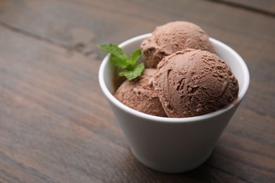 Photo of Bowl with tasty chocolate ice cream and mint leaves on wooden table. Space for text