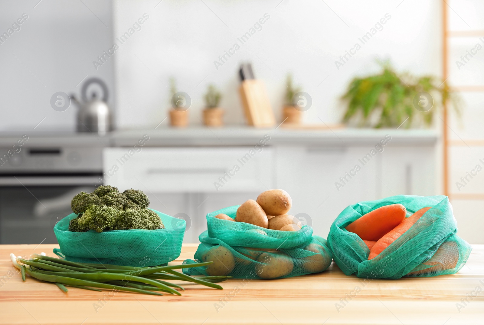 Photo of Net bags with vegetables on wooden table in kitchen