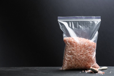 Photo of Pink himalayan salt in plastic bag on table against dark background, space for text