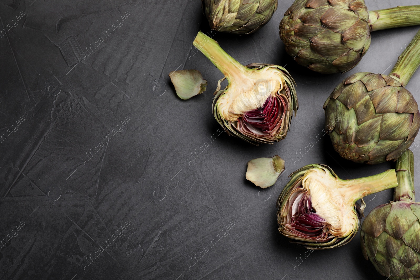 Photo of Cut and whole fresh raw artichokes on grey table, flat lay. Space for text