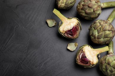 Cut and whole fresh raw artichokes on grey table, flat lay. Space for text