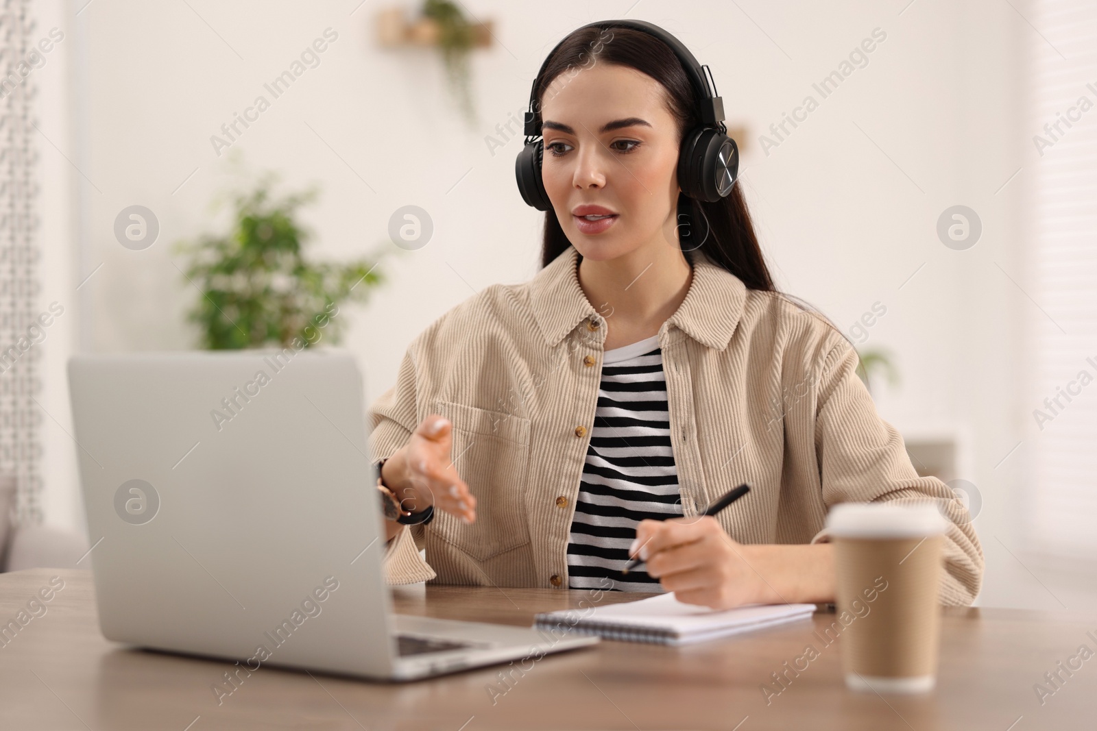 Photo of Young woman in headphones using video chat during webinar at table in room