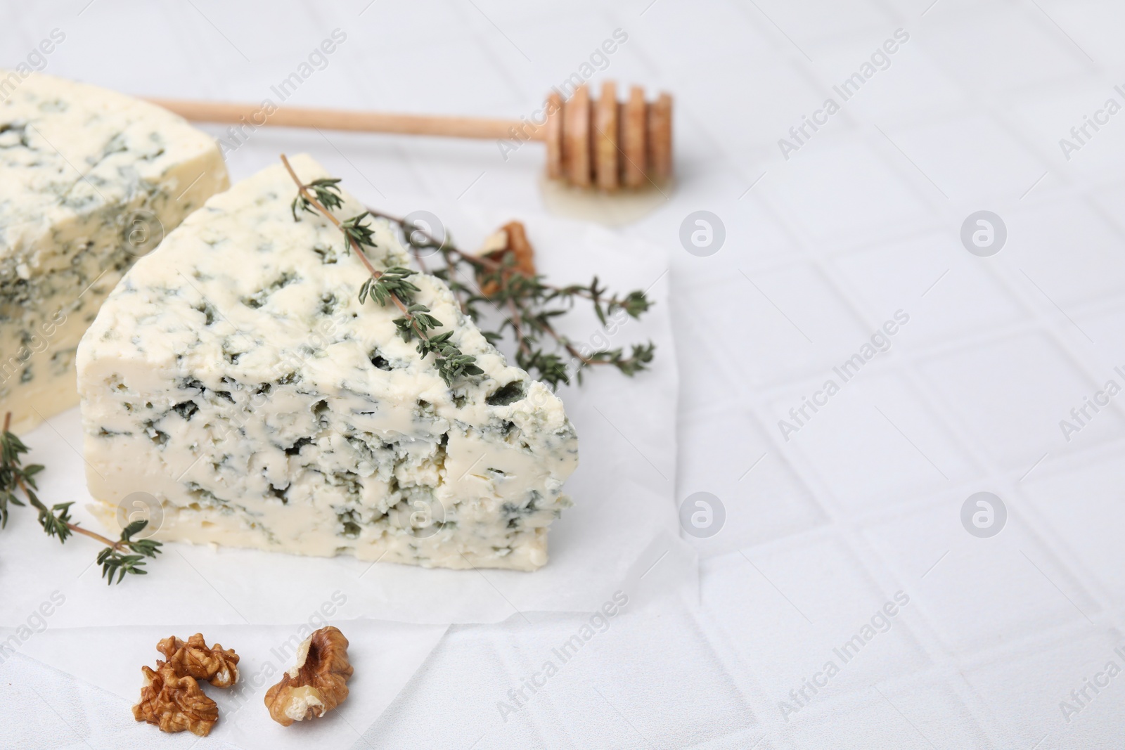 Photo of Tasty blue cheese with thyme, walnuts and honey dipper on white tiled table, closeup. Space for text