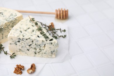 Tasty blue cheese with thyme, walnuts and honey dipper on white tiled table, closeup. Space for text