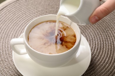 Photo of Woman pouring milk into cup with aromatic tea at table, closeup