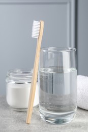 Bamboo toothbrush, glass of water and jar of baking soda on light grey table