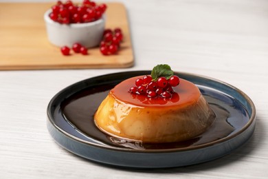 Plate of delicious caramel pudding with red currants and mint on white wooden table
