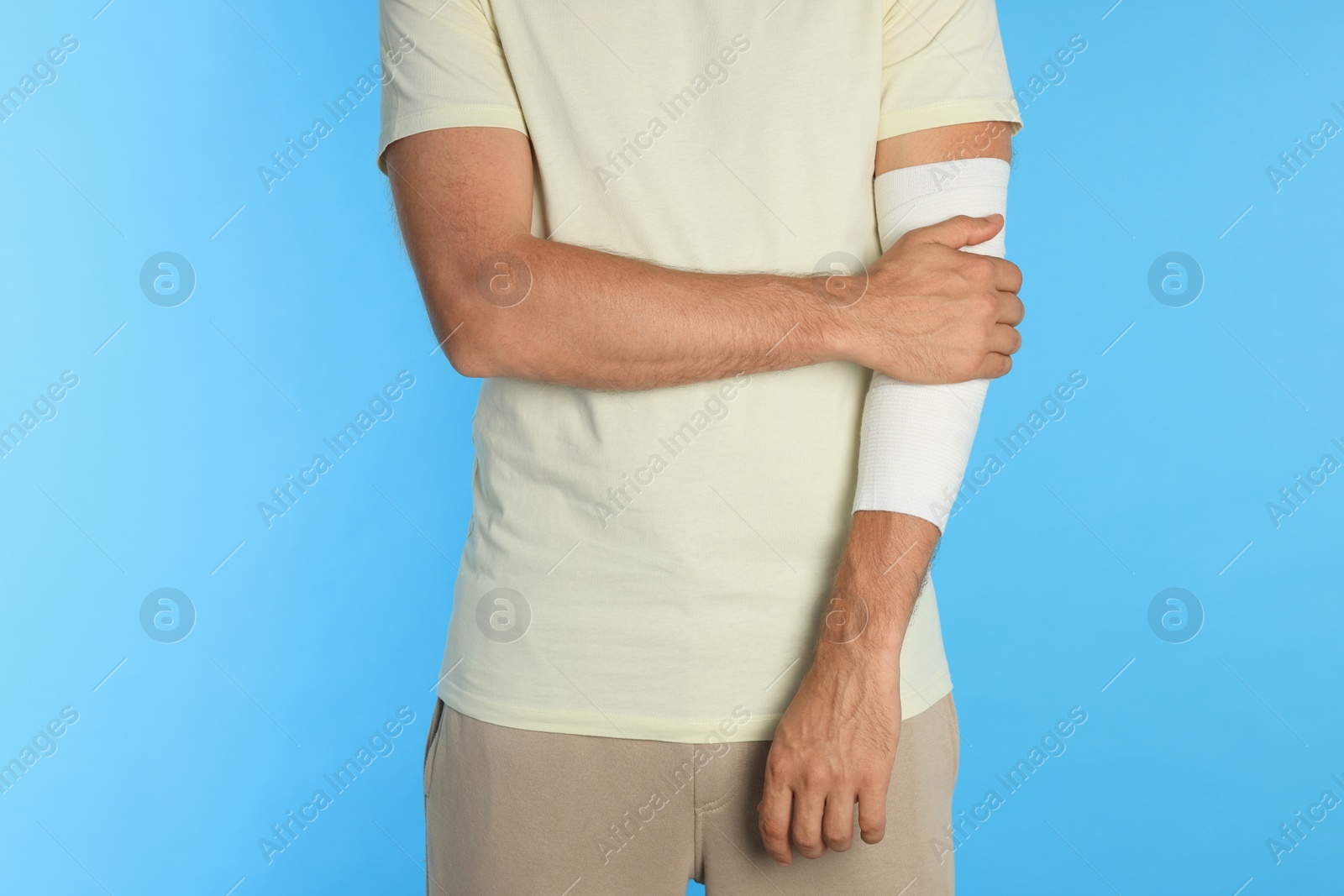 Photo of Man with arm wrapped in medical bandage on light blue background, closeup