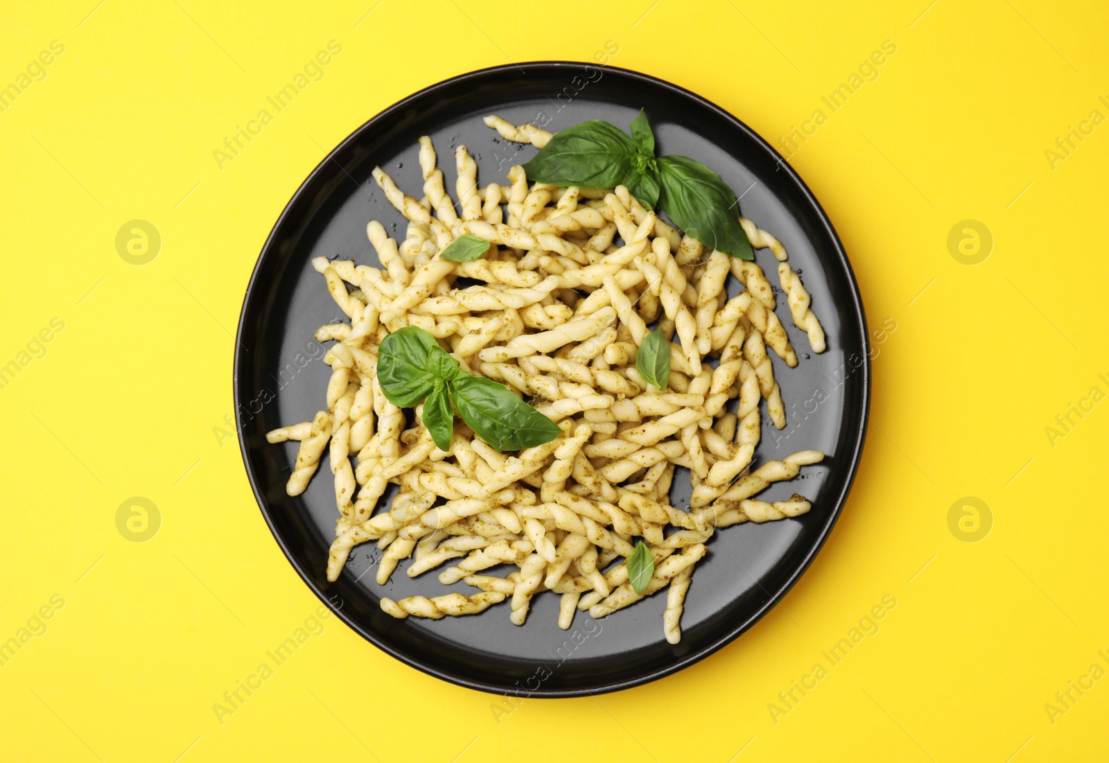 Photo of Plate of delicious trofie pasta with pesto sauce and basil leaves on yellow background, top view