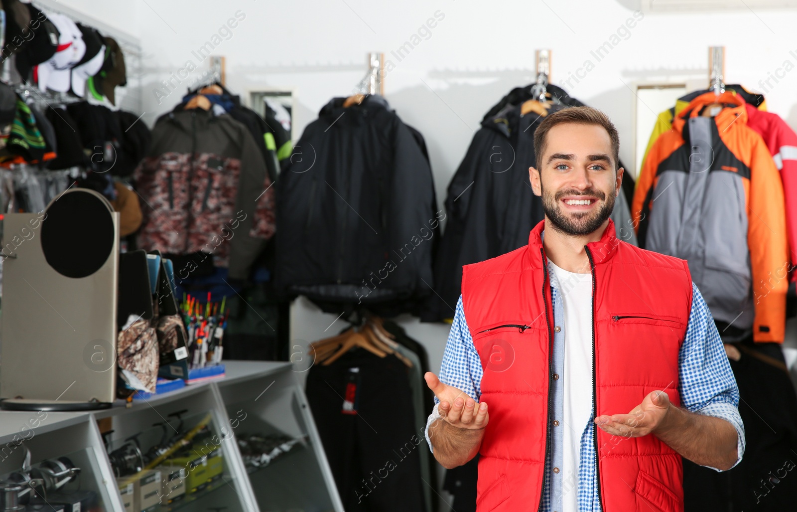Photo of Salesman standing near hangers with fishing clothing in sports shop. Space for text