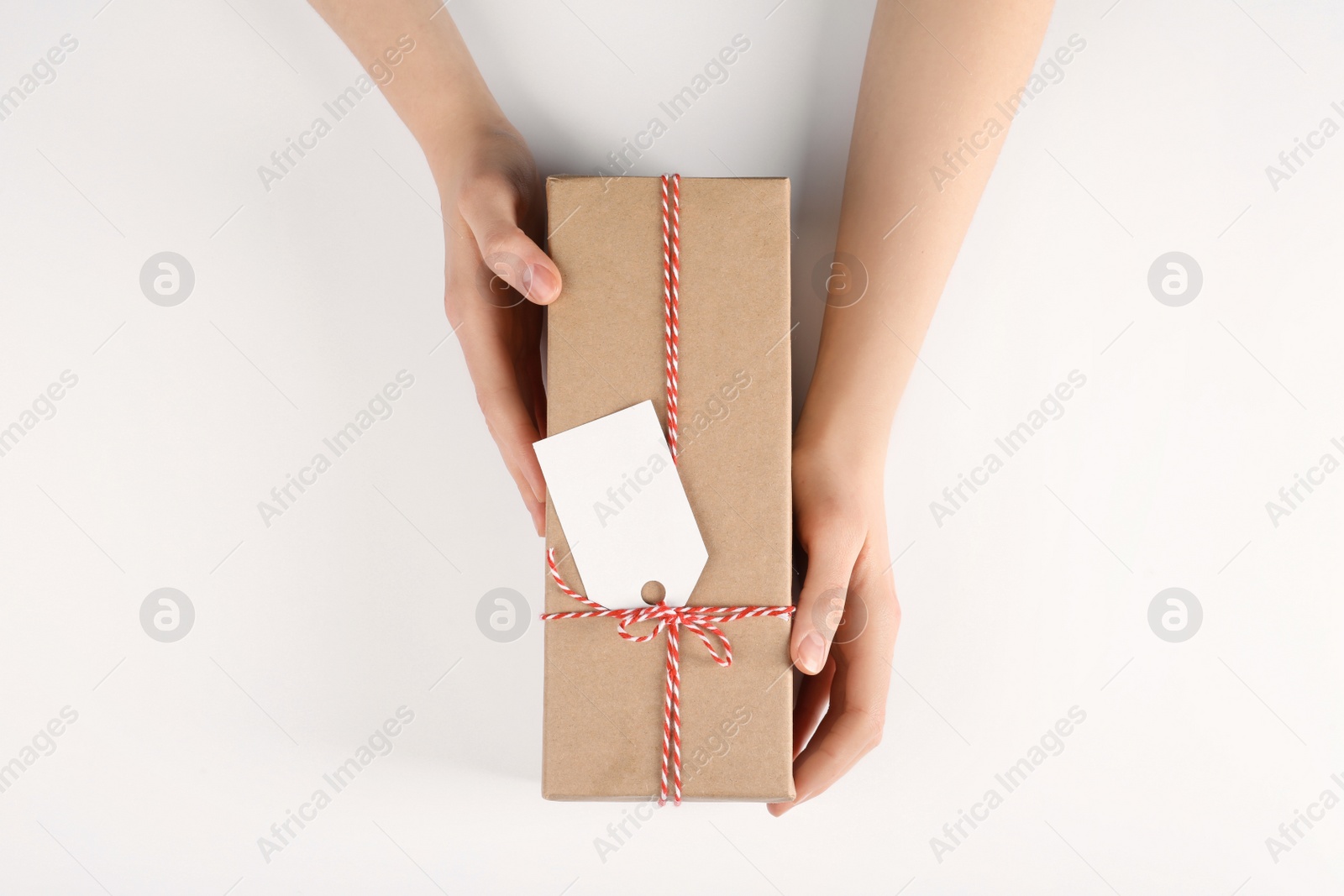 Photo of Woman holding parcel wrapped in kraft paper with tag on white background, top view