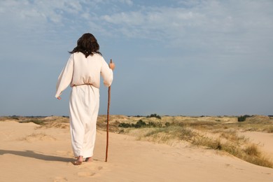 Photo of Jesus Christ walking with stick in desert, back view. Space for text