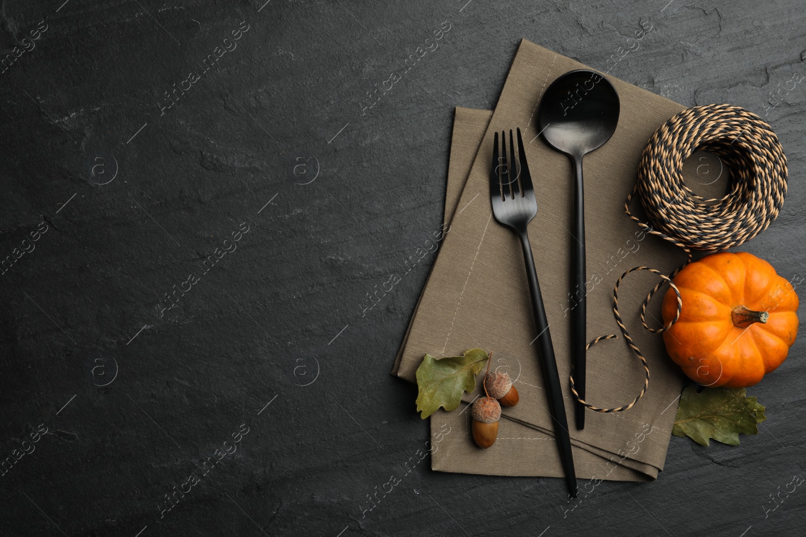 Photo of Cutlery, pumpkin and rope on black slate background, flat lay with space for text. Table setting elements