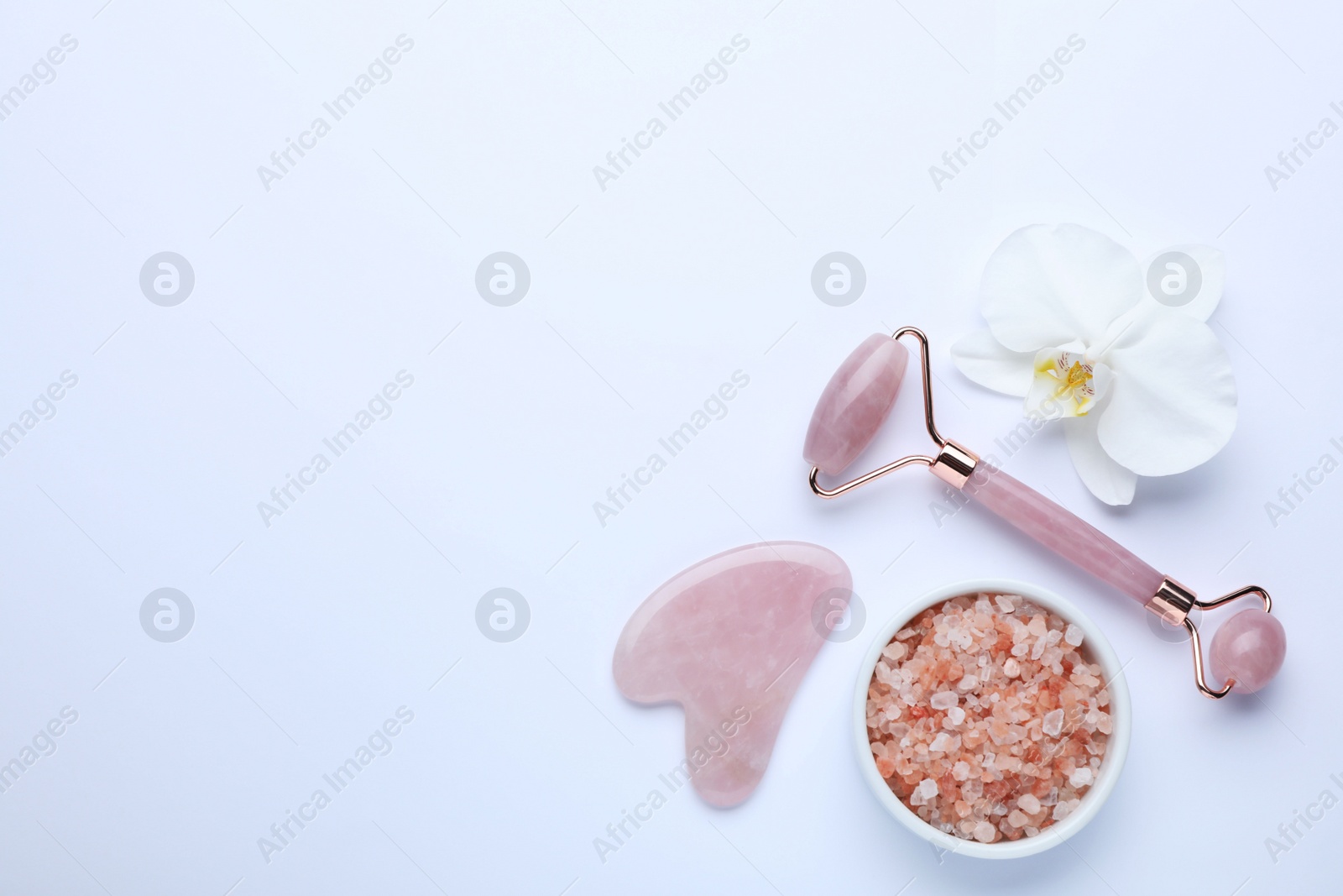 Photo of Gua sha stone, face roller, bath salt and orchid flower on white background, flat lay. Space for text