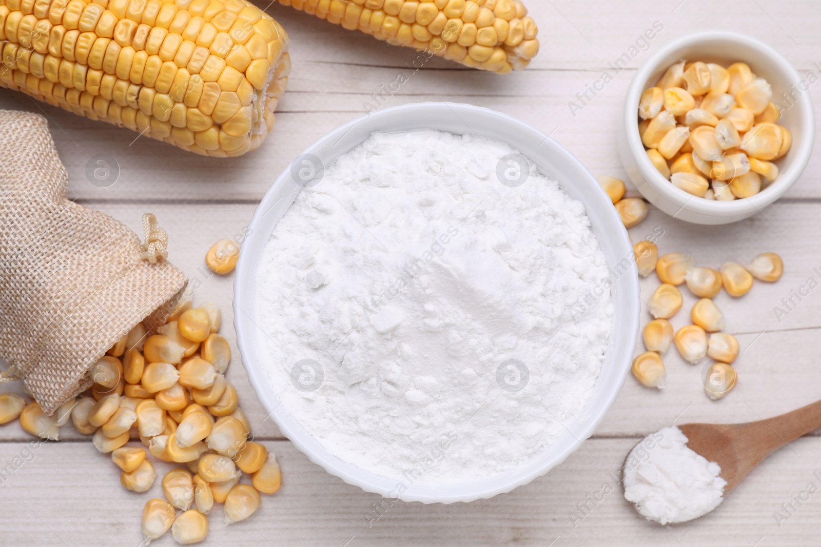 Photo of Bowl with corn starch, ripe cobs and kernels on wooden table, flat lay