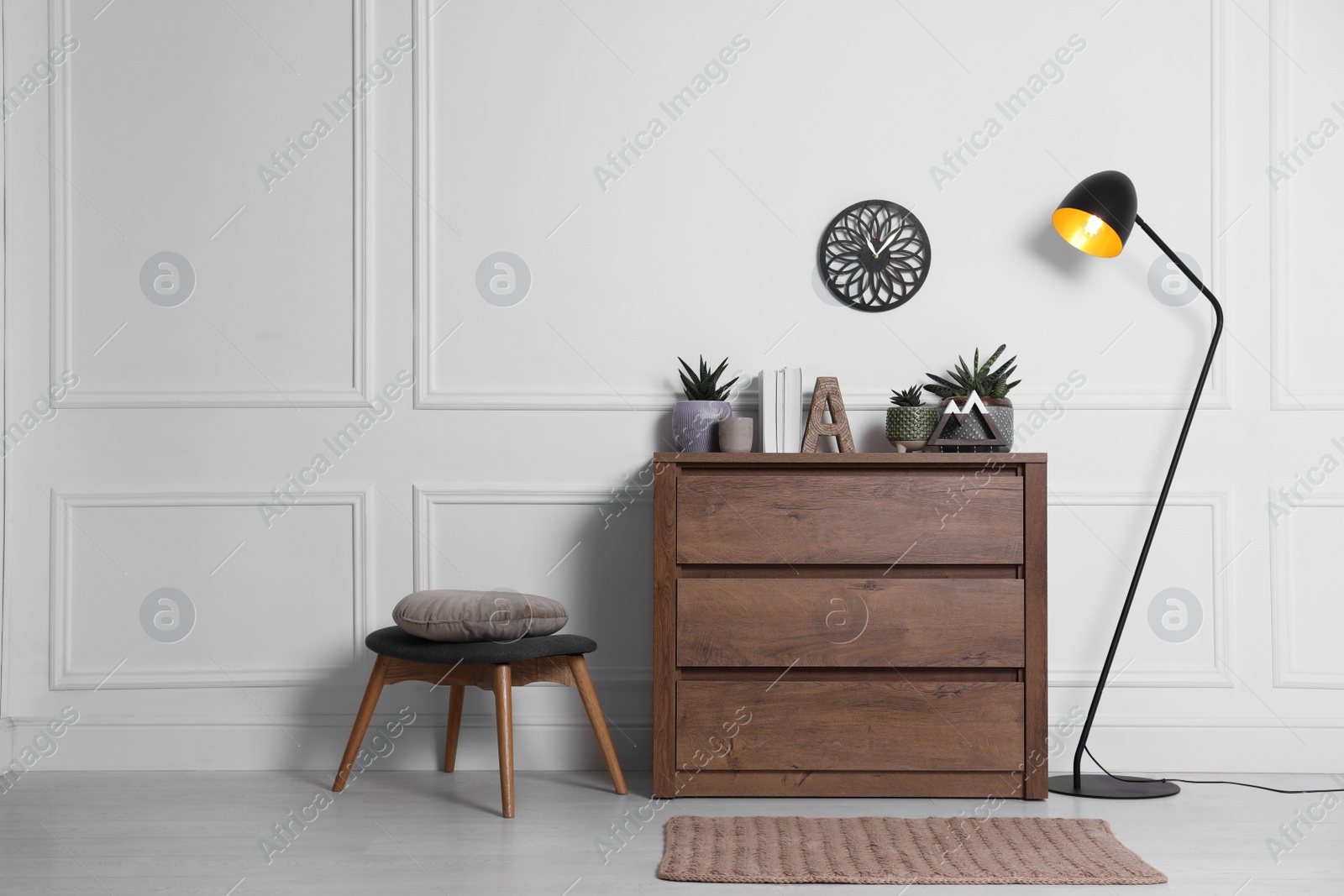 Photo of Stylish room interior with wooden chest of drawers near white wall