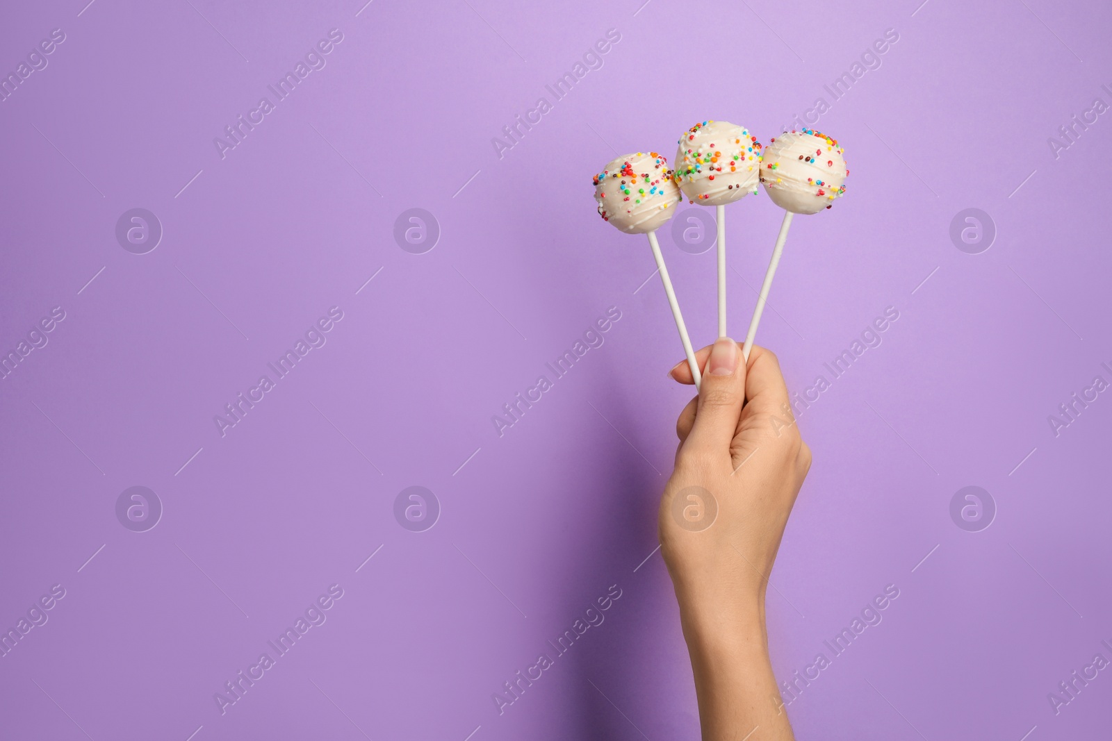 Photo of Woman holding bright delicious cake pops on color background, closeup. Space for text