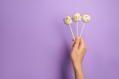 Photo of Woman holding bright delicious cake pops on color background, closeup. Space for text