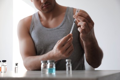 Athletic man filling syringe at table indoors, closeup. Doping concept