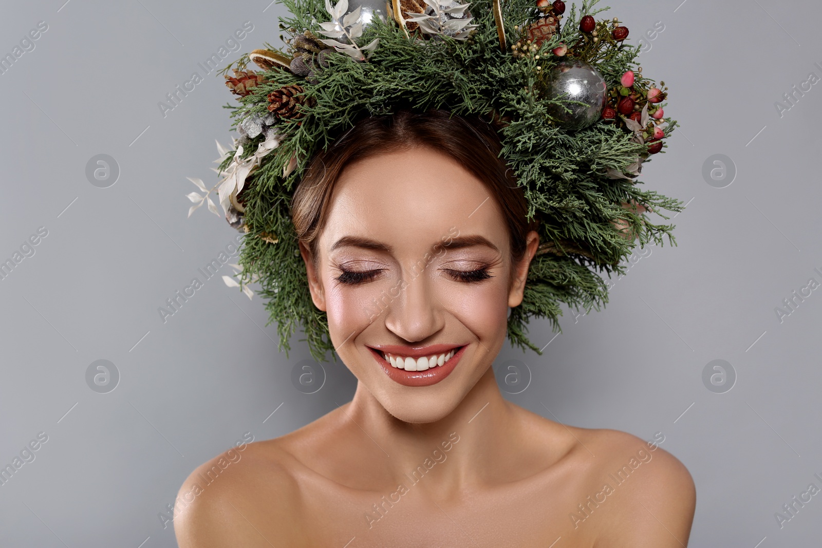 Photo of Beautiful young woman wearing Christmas wreath on grey background