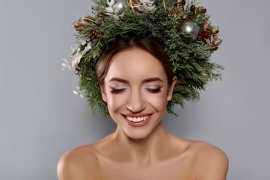 Beautiful young woman wearing Christmas wreath on grey background