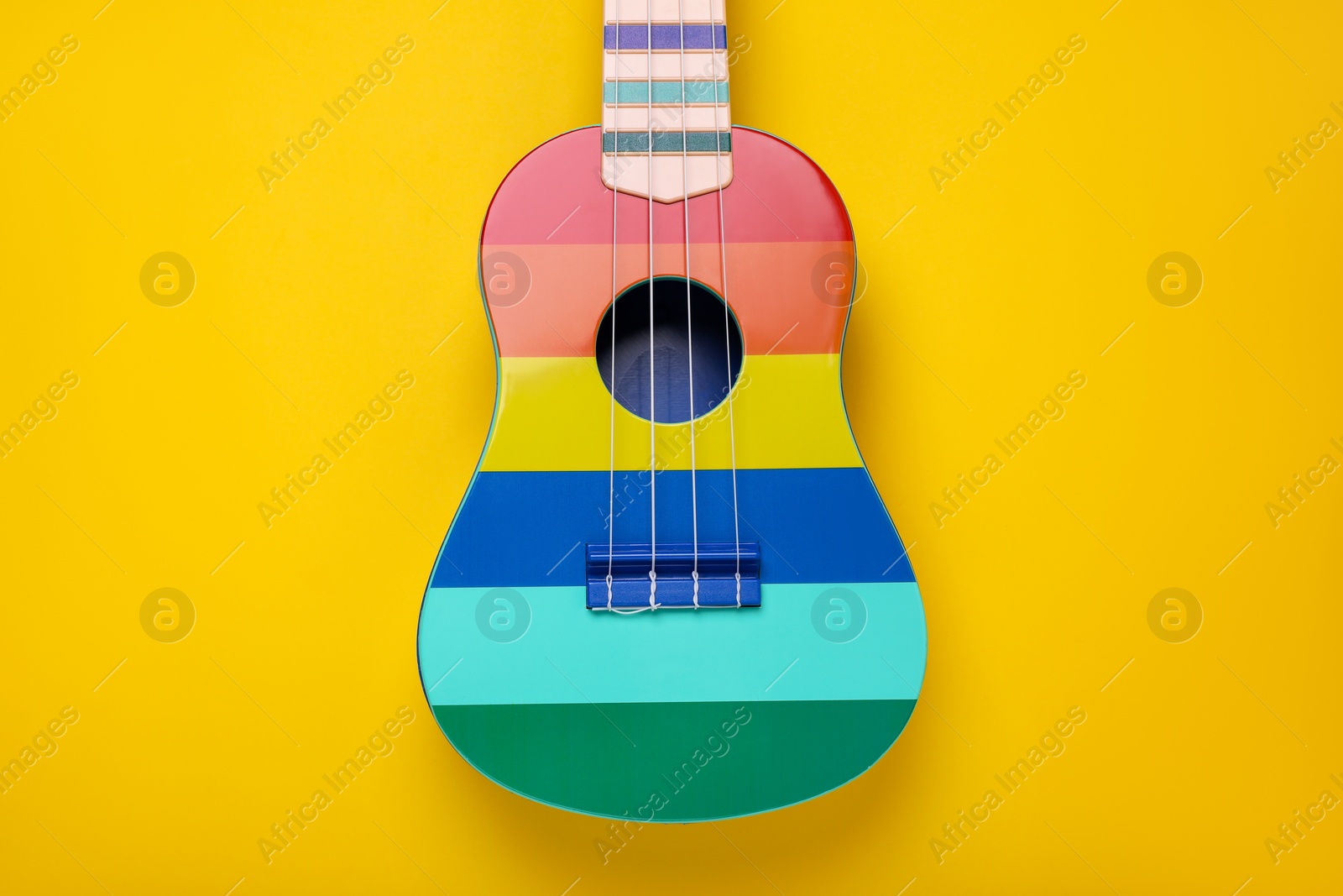 Photo of Colorful ukulele on yellow background, top view. String musical instrument