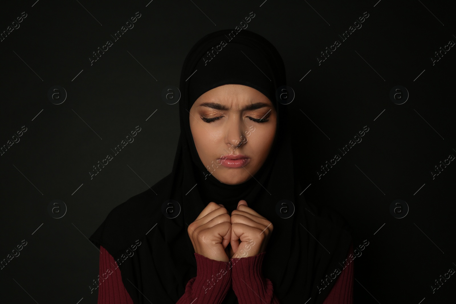 Photo of Portrait of sad Muslim woman in hijab  praying on dark background