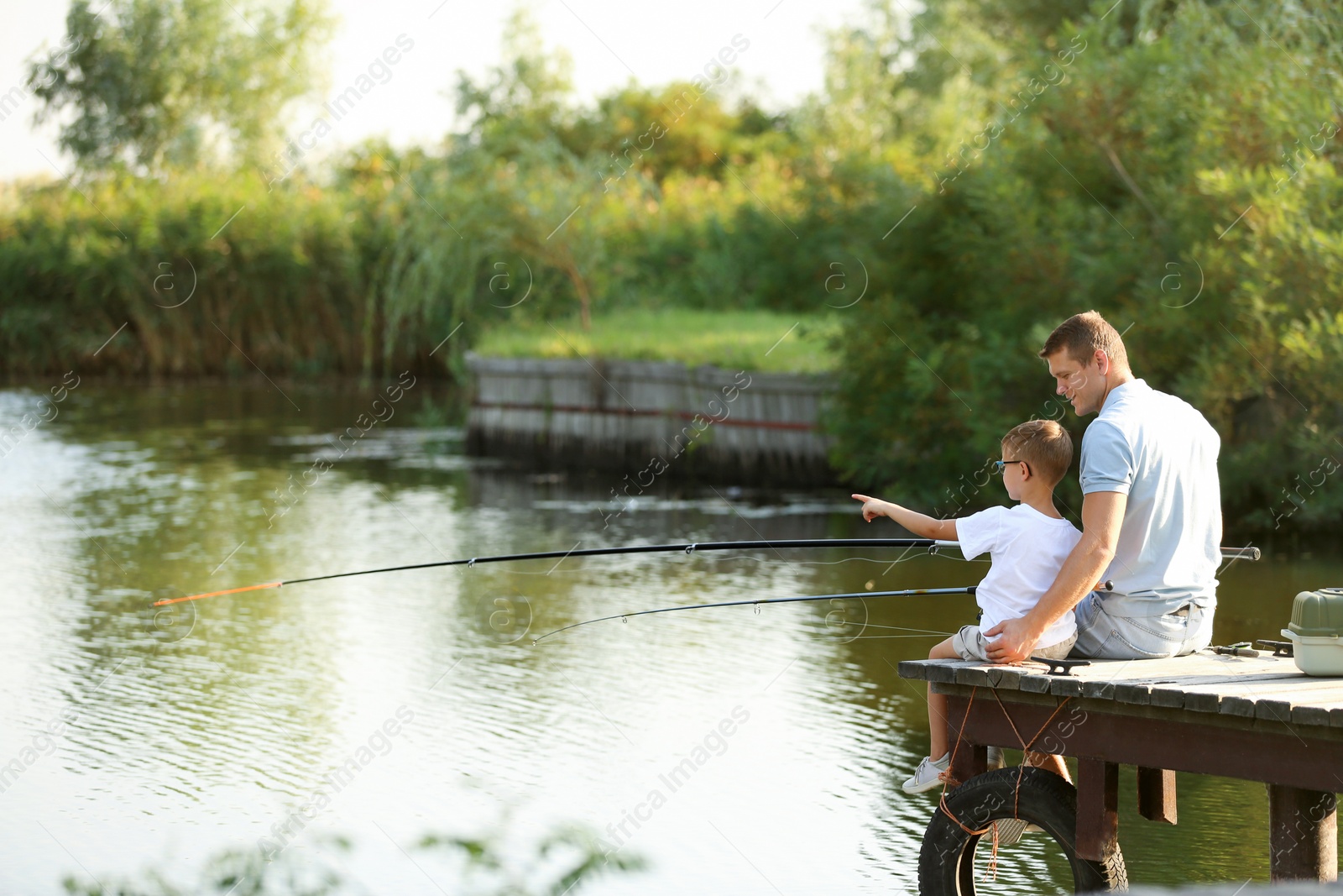 Photo of Dad and son fishing together on sunny day. Space for text