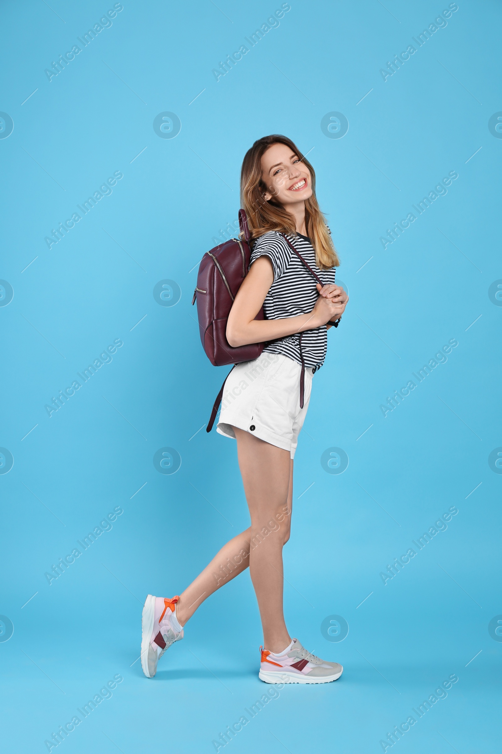 Photo of Happy woman with backpack on light blue background