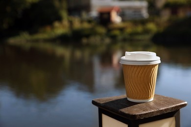 Photo of Takeaway paper cup with coffee near river outdoors. Space for text