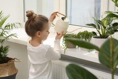 Photo of Cute little girl watering beautiful green plant on windowsill at home. House decor