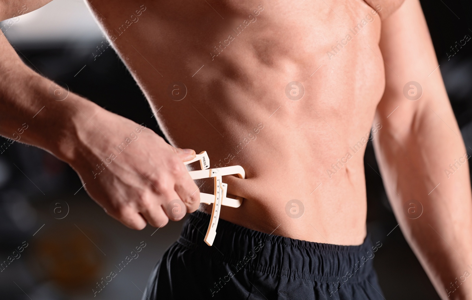 Photo of Man measuring body fat layer with caliper indoors, closeup