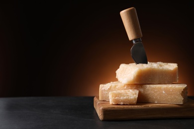 Photo of Delicious parmesan cheese with knife on black table. Space for text