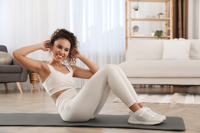 Photo of Beautiful African American woman doing abs exercise on yoga mat at home