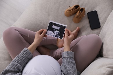 Photo of Young pregnant woman with ultrasound picture of baby on sofa, above view