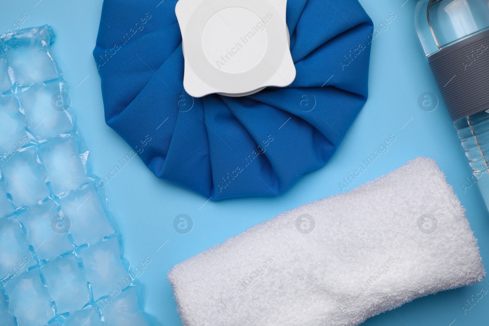 Photo of Bottle of water, cold compress, ice pack and towel on light blue background, flat lay. Heat stroke treatment