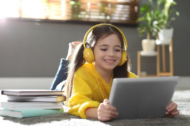 Photo of Cute little girl with headphones and tablet listening to audiobook at home