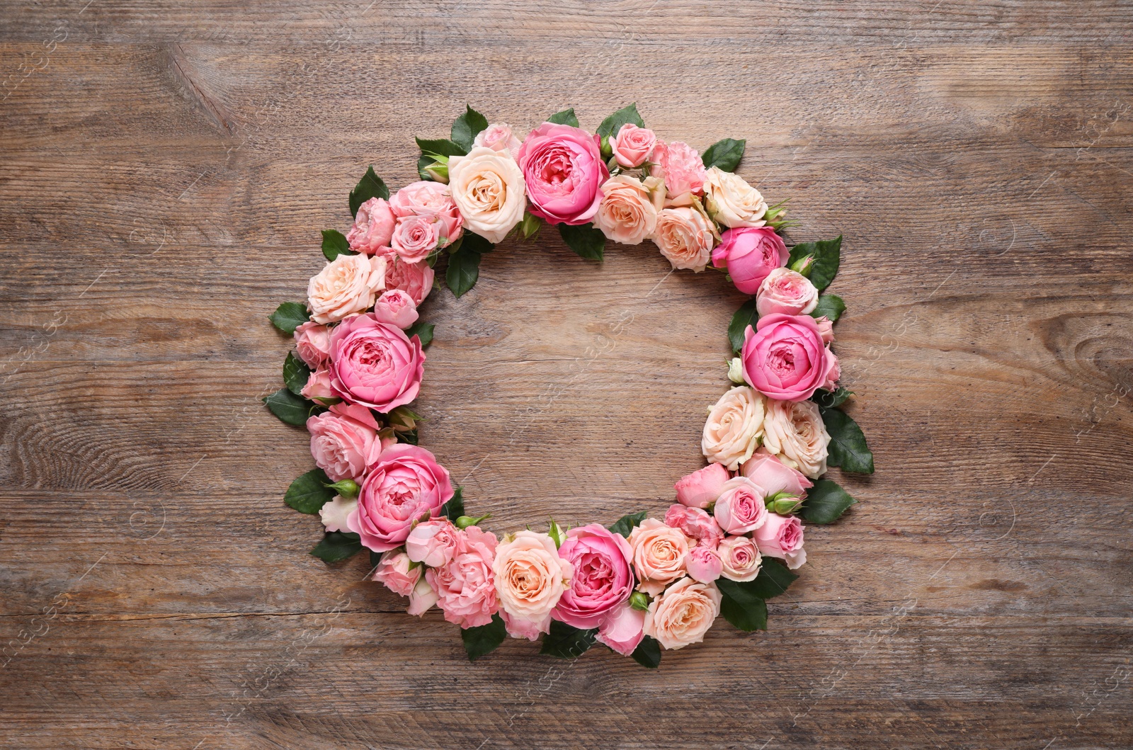 Photo of Wreath made of beautiful rose flowers and green leaves on wooden background, flat lay. Space for text