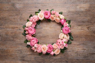 Wreath made of beautiful rose flowers and green leaves on wooden background, flat lay. Space for text