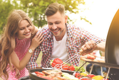 Young couple having barbecue with modern grill outdoors